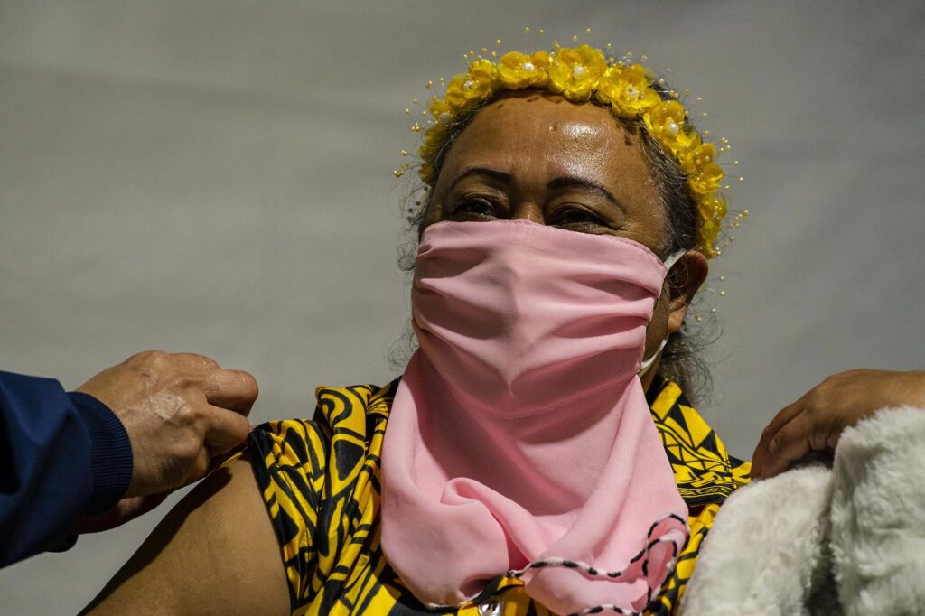 Triscilla Cleland, wearing a traditional outfit representing her native island of Chuuk in Micronesia, receives a COVID-19 vaccination.