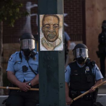 A portrait of George Floyd hangs on a street light pole as police officers stand guard.