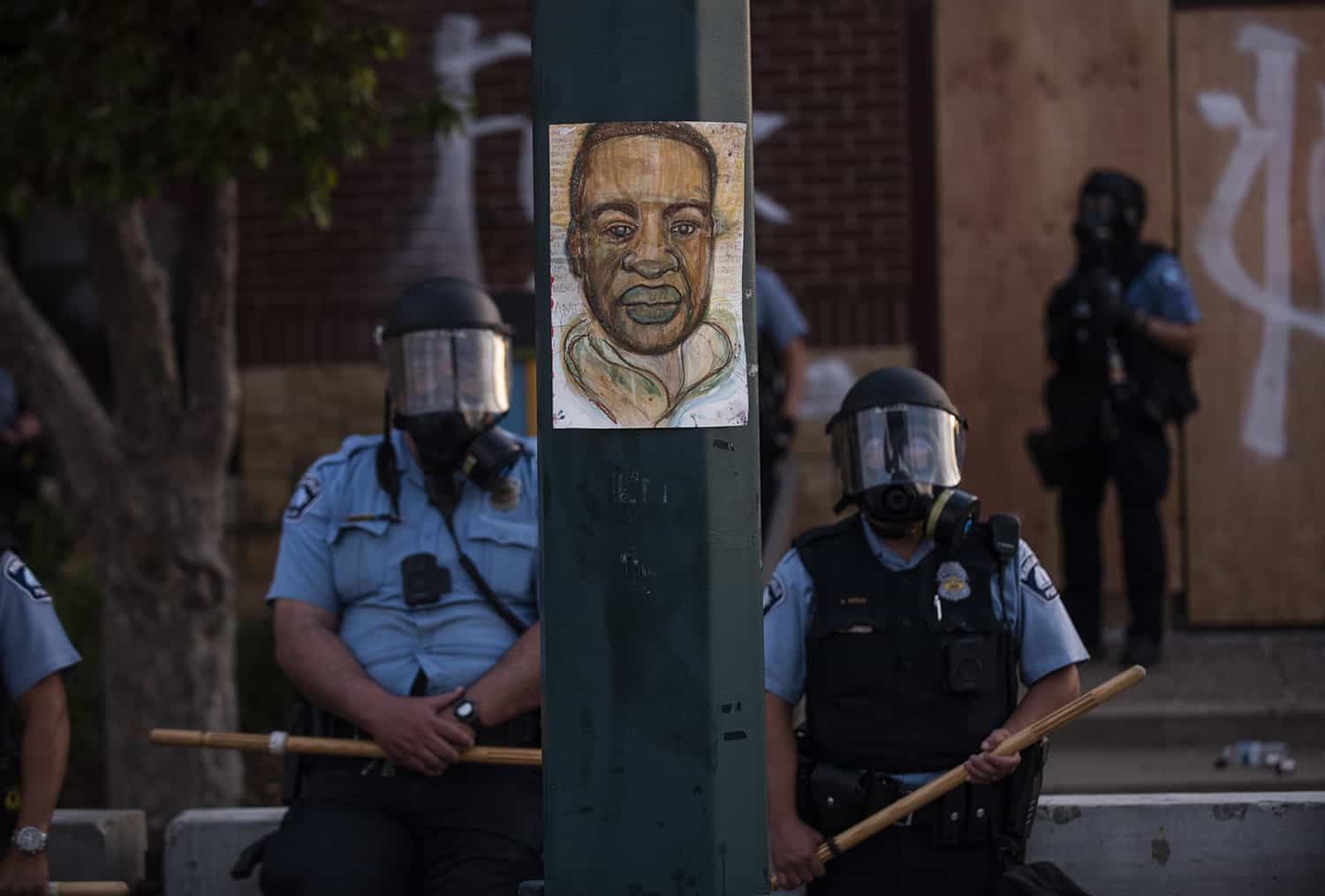 A portrait of George Floyd hangs on a street light pole as police officers stand guard.