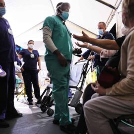 Clinicians evaluate an incoming patient with his arms raised in a triage tent set up in the parking lot at Providence St. Mary Medical Center amid a surge in COVID-19 patients.